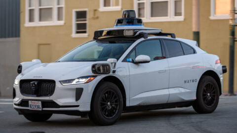 White Waymo Jaguar I-Pace robotaxi with roof sensors driving on a city street