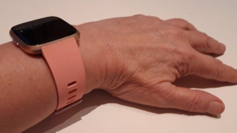 A Fitbit fitness tracker with a pink band worn on a wrist