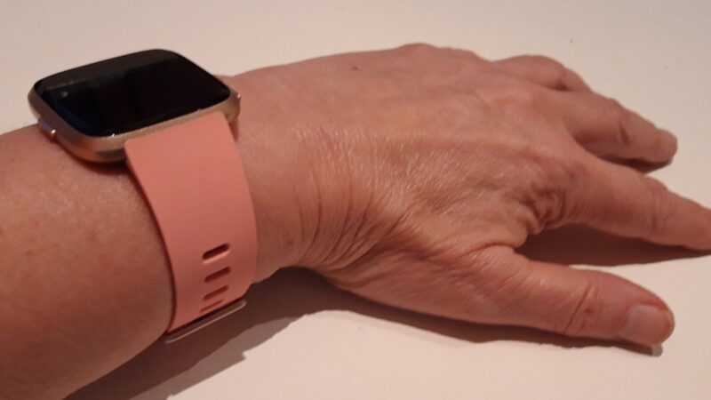 A Fitbit fitness tracker with a pink band worn on a wrist