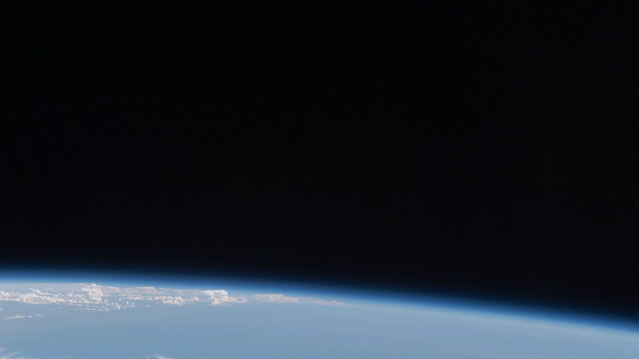 A white crew capsule spacecraft approaching in orbit above Earth's cloud-covered horizon