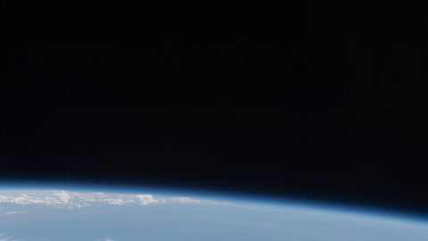 A white crew capsule spacecraft approaching in orbit above Earth's cloud-covered horizon
